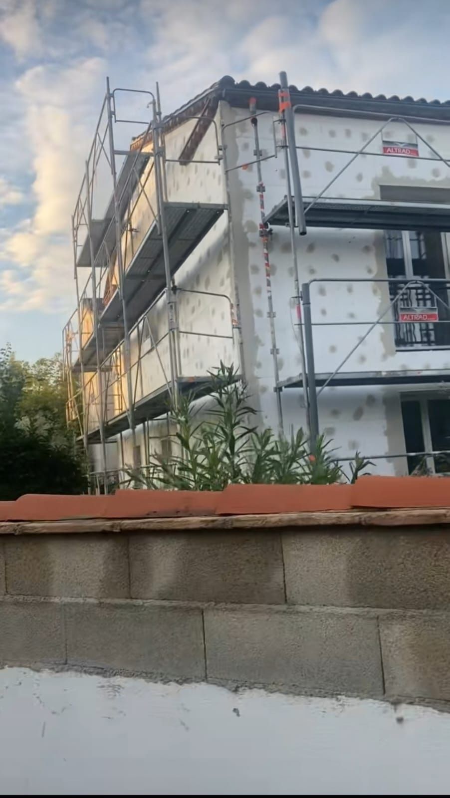 Exterior del edificio en construcción; andamios, paneles aislantes, pared de ladrillo en primer plano.