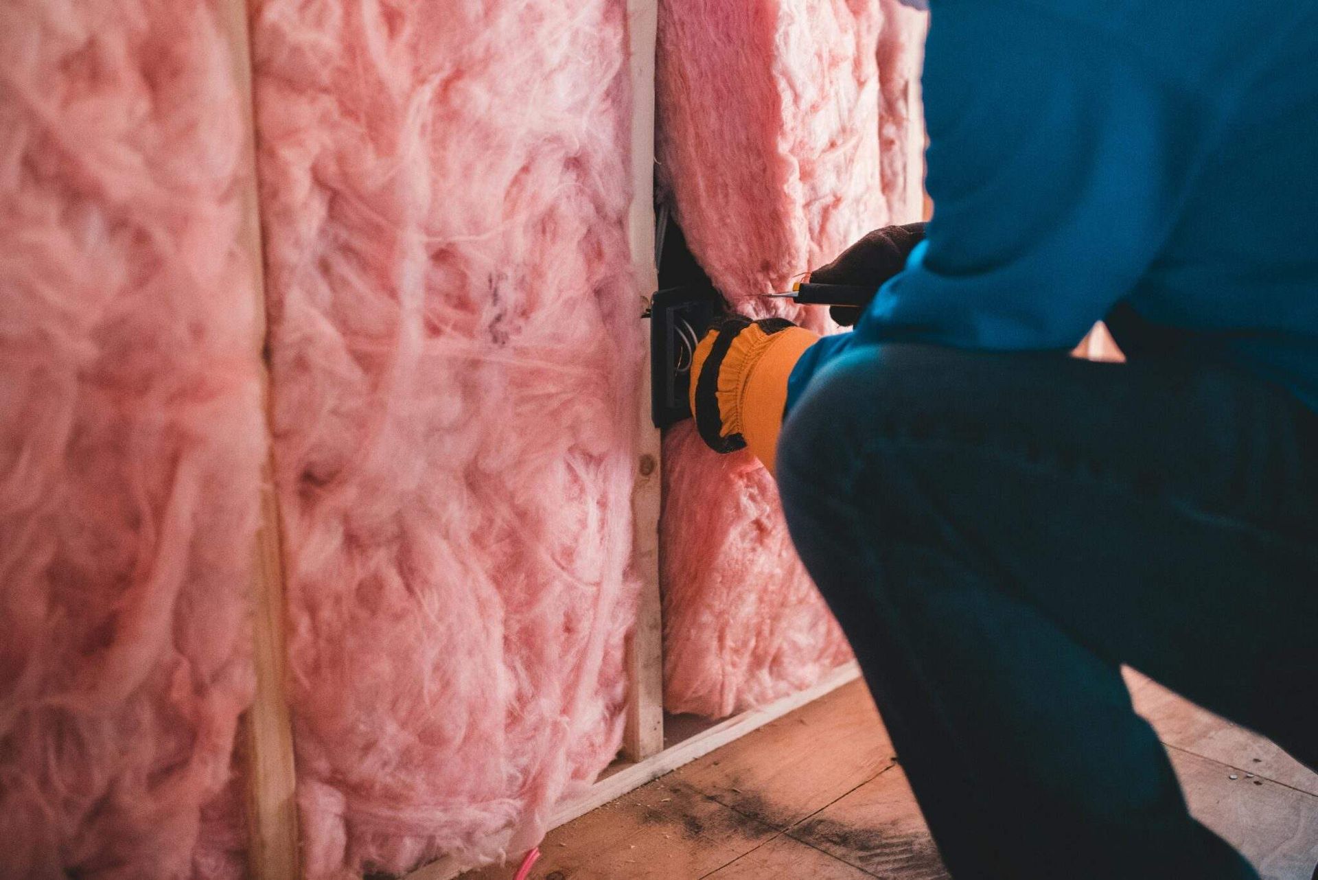 Persona instalando aislamiento rosa en un marco de pared de madera con una herramienta amarilla.