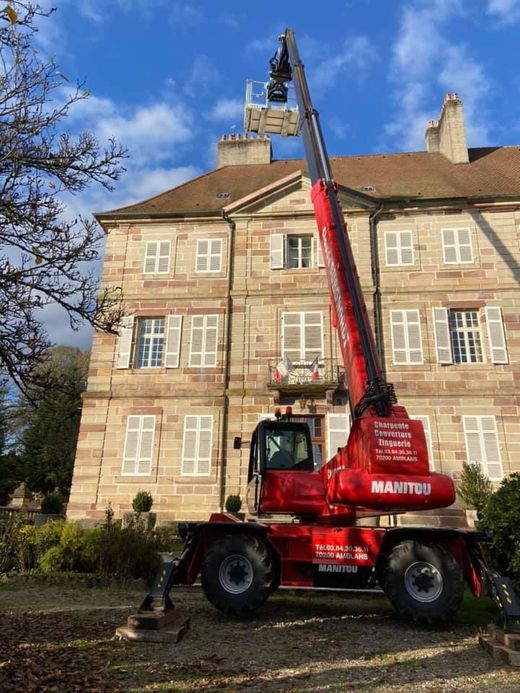 Une grue rouge soulève une nacelle à côté d'un bâtiment en pierre beige sous un ciel bleu.