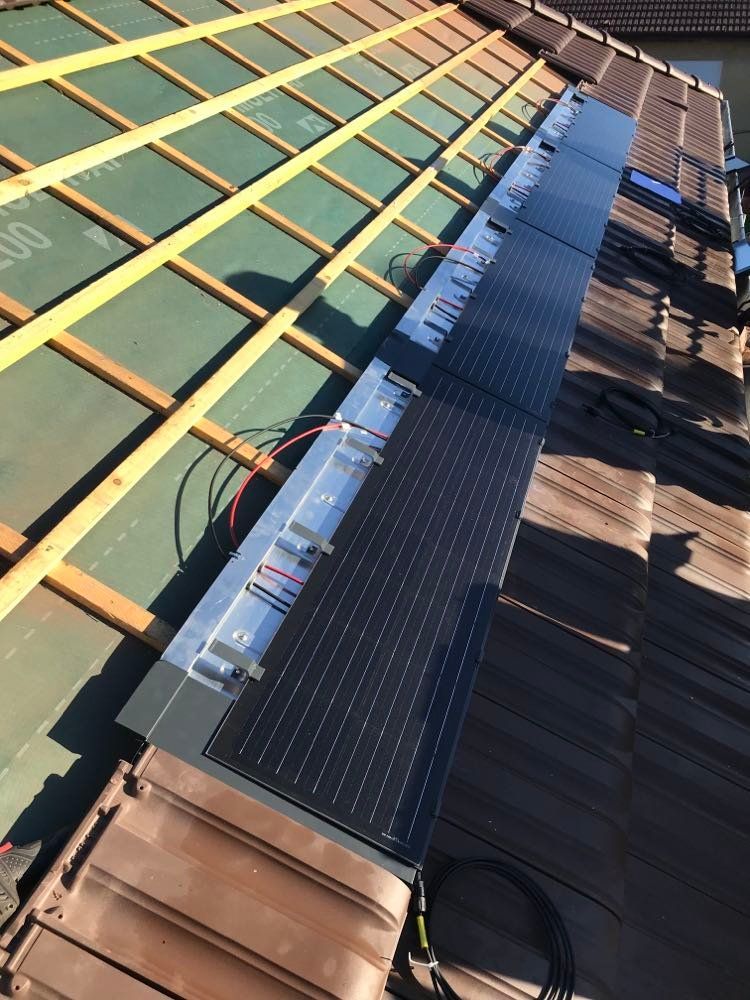 Des panneaux solaires sont installés le long d'une crête de toit, à côté d'un toit teinté en vert et de bardeaux bruns.