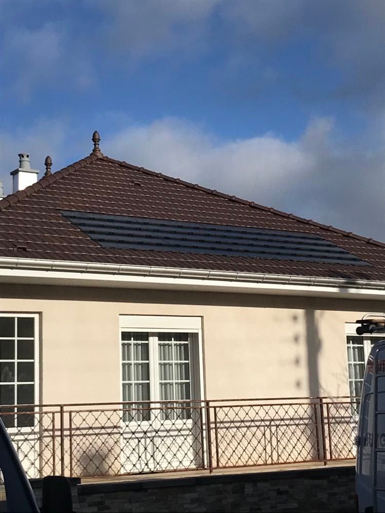 Maison beige de plain-pied avec toit de tuiles brunes, panneaux solaires et balustrade de balcon en métal sous un ciel bleu