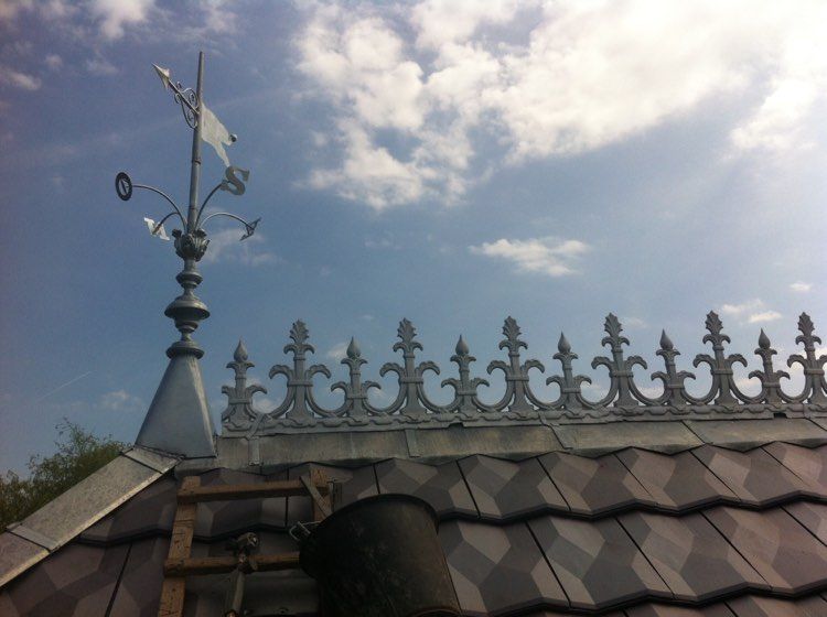 Girouette ornée sur le toit et garnitures en fer forgé se détachant sur un ciel bleu partiellement nuageux