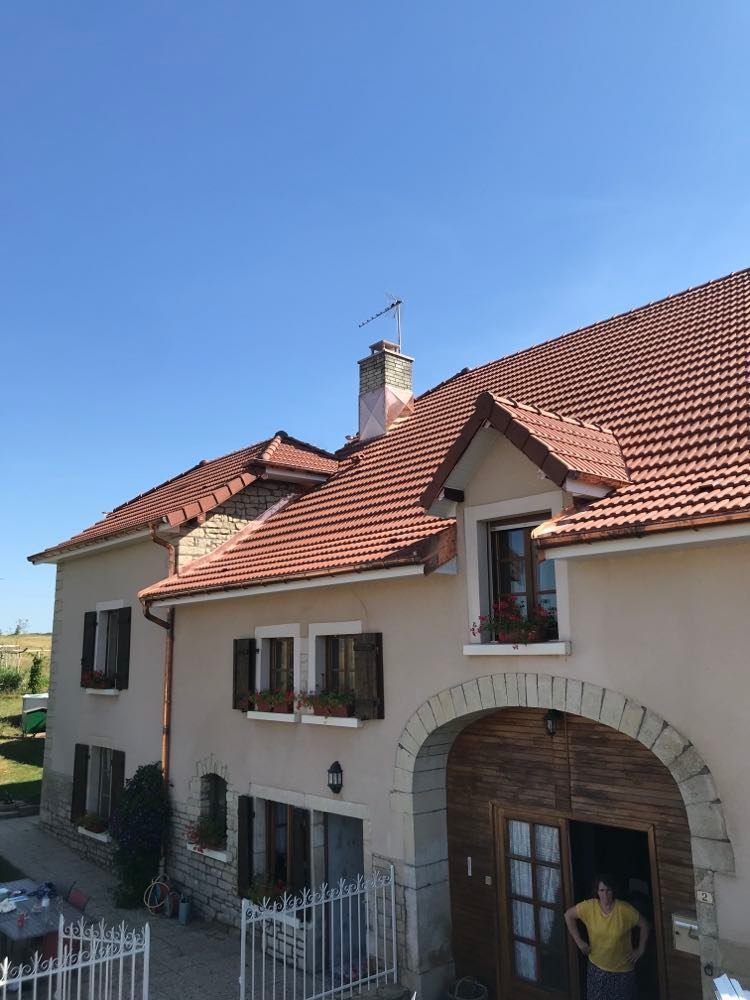 Maison à deux étages avec toit de tuiles rouges et entrée voûtée par une journée ensoleillée