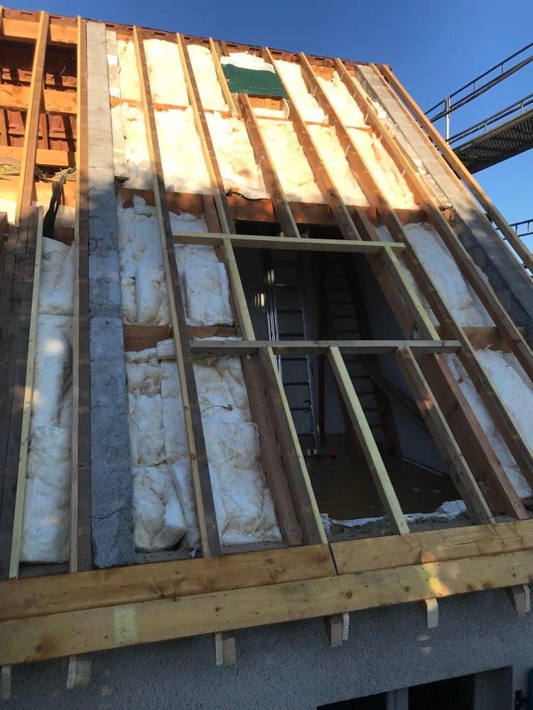 Extérieur d'une maison partiellement ossature bois, avec isolation apparente et ouvertures de fenêtres ouvertes, en construction