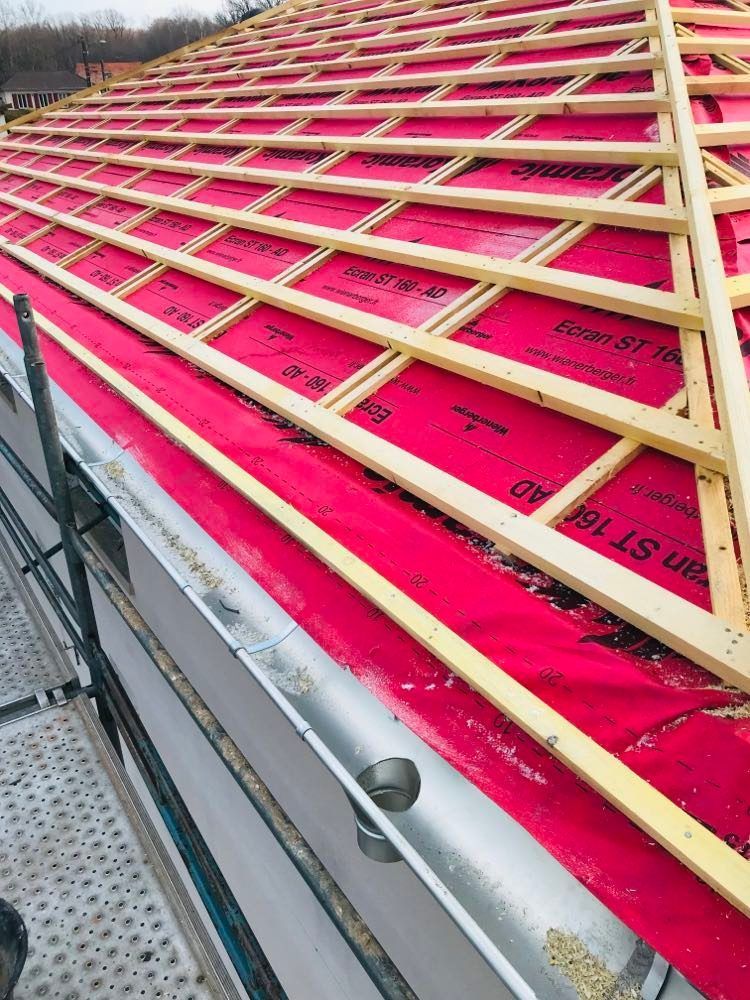 Toiture isolée rose vif avec charpente en treillis de bois beige sur un chantier de construction.