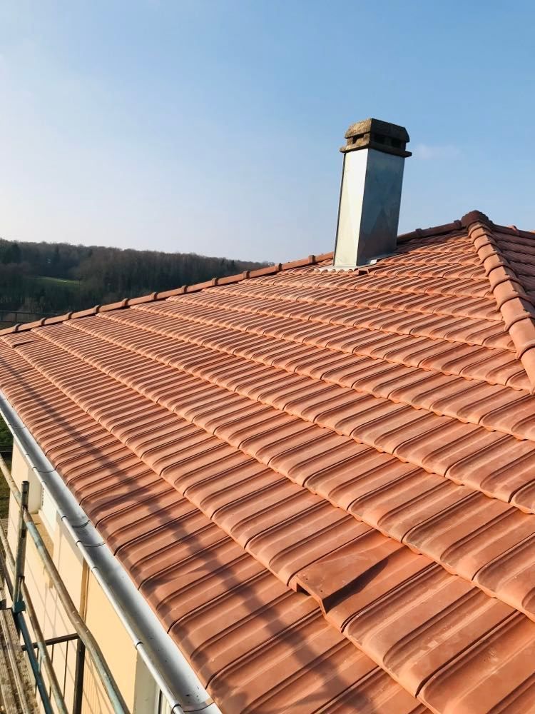 Toit de tuiles en terre cuite rouge avec une cheminée sous un ciel bleu clair