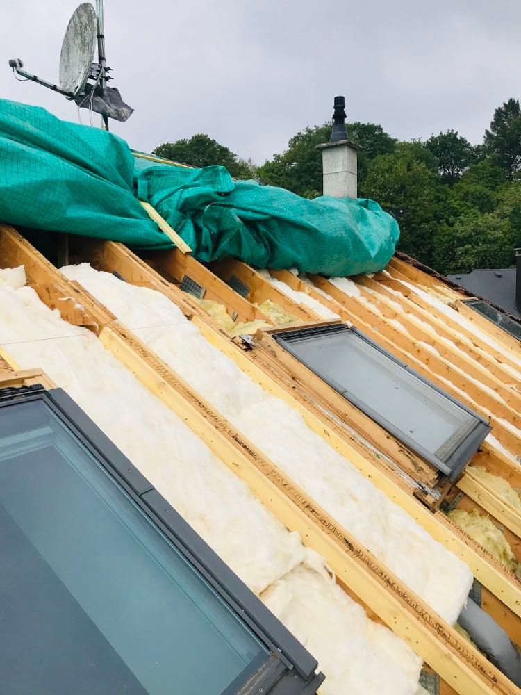 Toiture endommagée avec isolation apparente, bâche verte et puits de lumière en cours de réparation