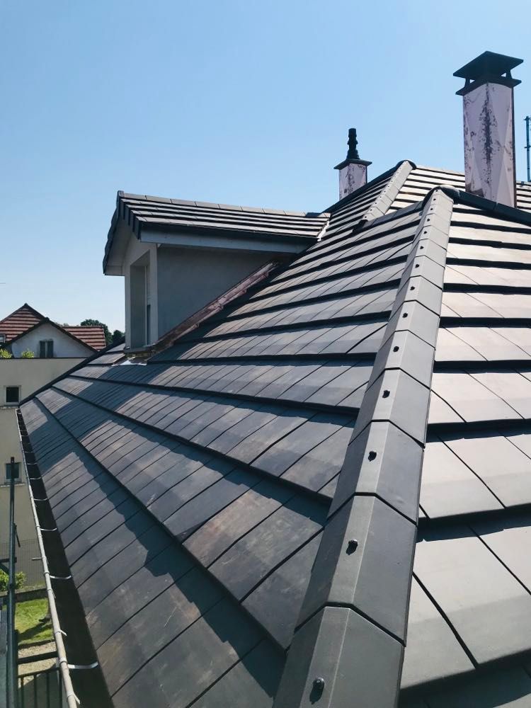 Toit d'habitation en ardoise avec cheminées sous un ciel bleu clair
