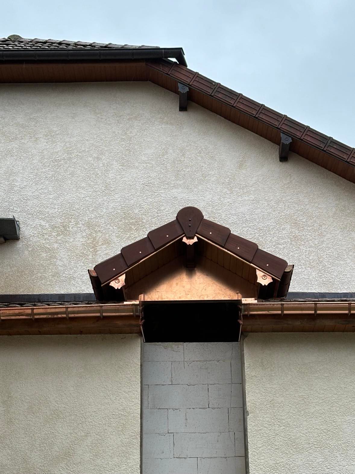 Pignon extérieur et toiture avec ornements bruns, enduit blanc et petite entrée couverte en dessous.