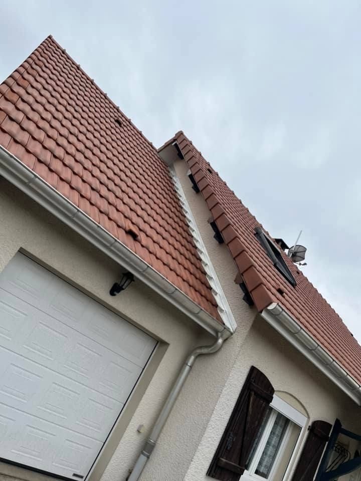 Toit de maison en tuiles rouges et porte de garage blanche, vus d'en bas sous un ciel nuageux