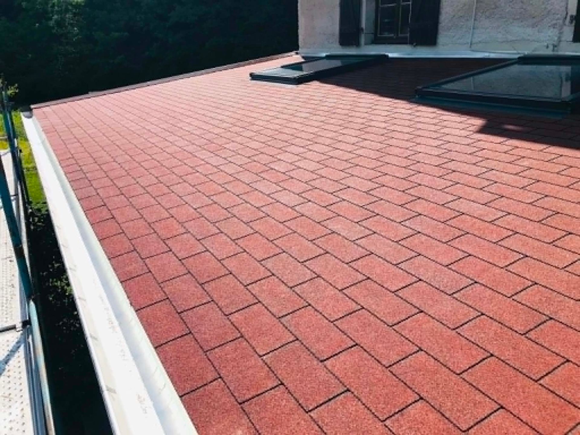 Terrasse sur le toit rouge avec des bardeaux rectangulaires et une rambarde blanche à côté d'un bâtiment