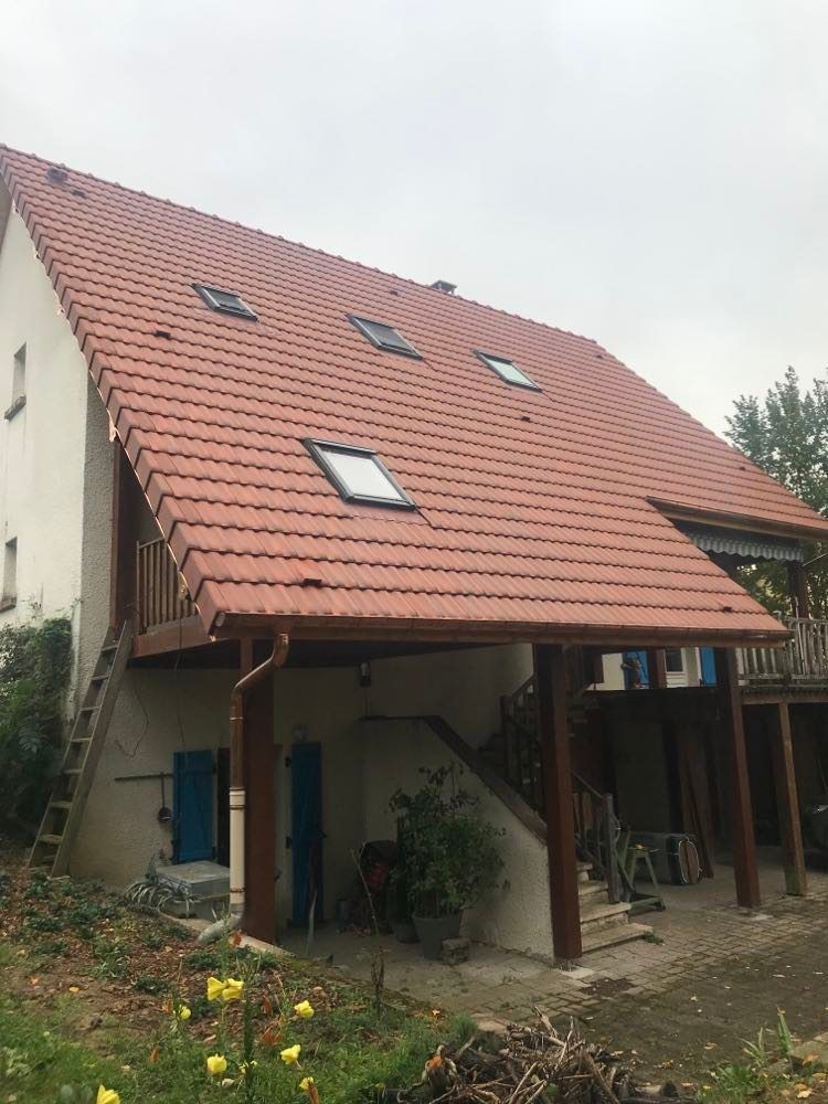 Maison à deux étages avec un toit de tuiles rouges, des puits de lumière et un patio couvert dans un cadre de jardin