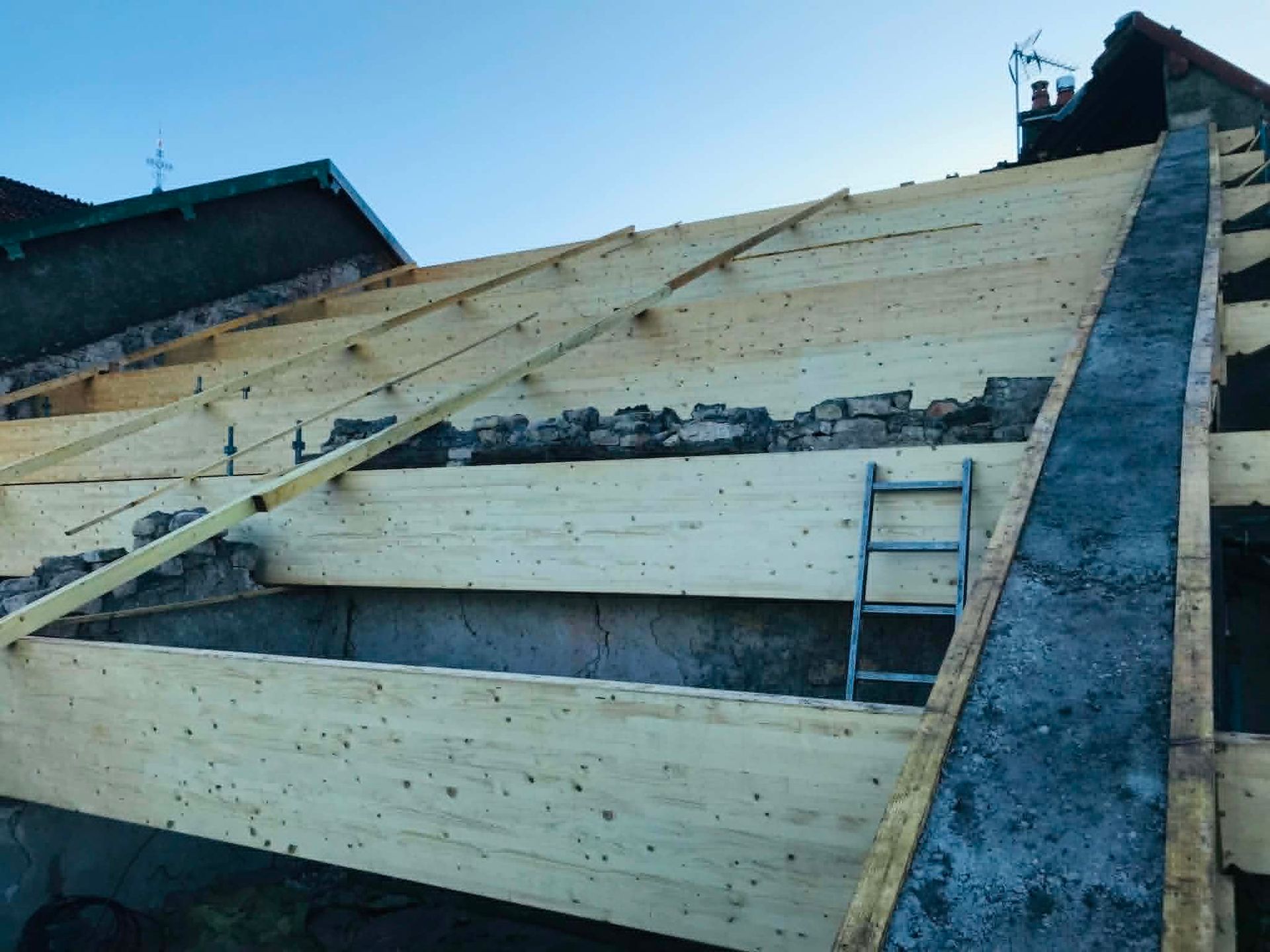 Toiture partiellement charpentée avec des planches de bois et une échelle sur une structure pentue en construction