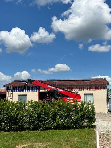 Grue rouge soulevant une charge sur un bâtiment clair sous un ciel bleu nuageux