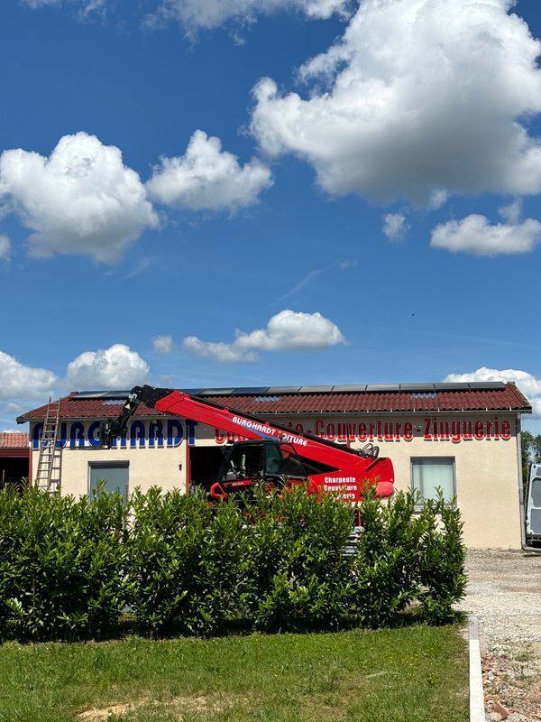Bâtiment rural avec un auvent rouge sous un ciel bleu nuageux, bordé d'arbustes verts.