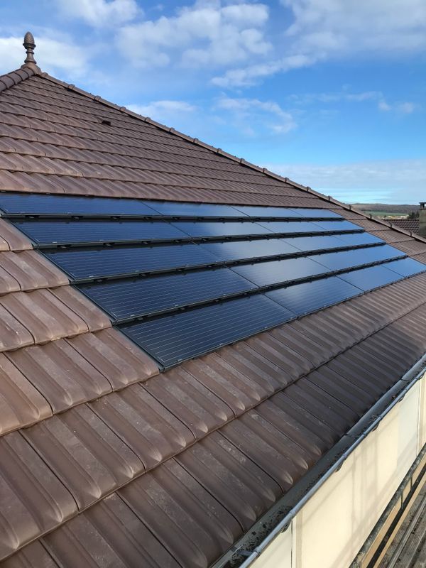 Des panneaux solaires installés sur un toit de tuiles brunes sous un ciel bleu.