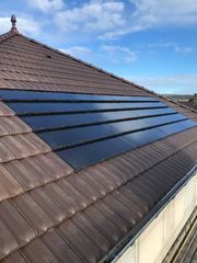 Toit en tuiles brunes et rangée de panneaux solaires noirs sous un ciel bleu