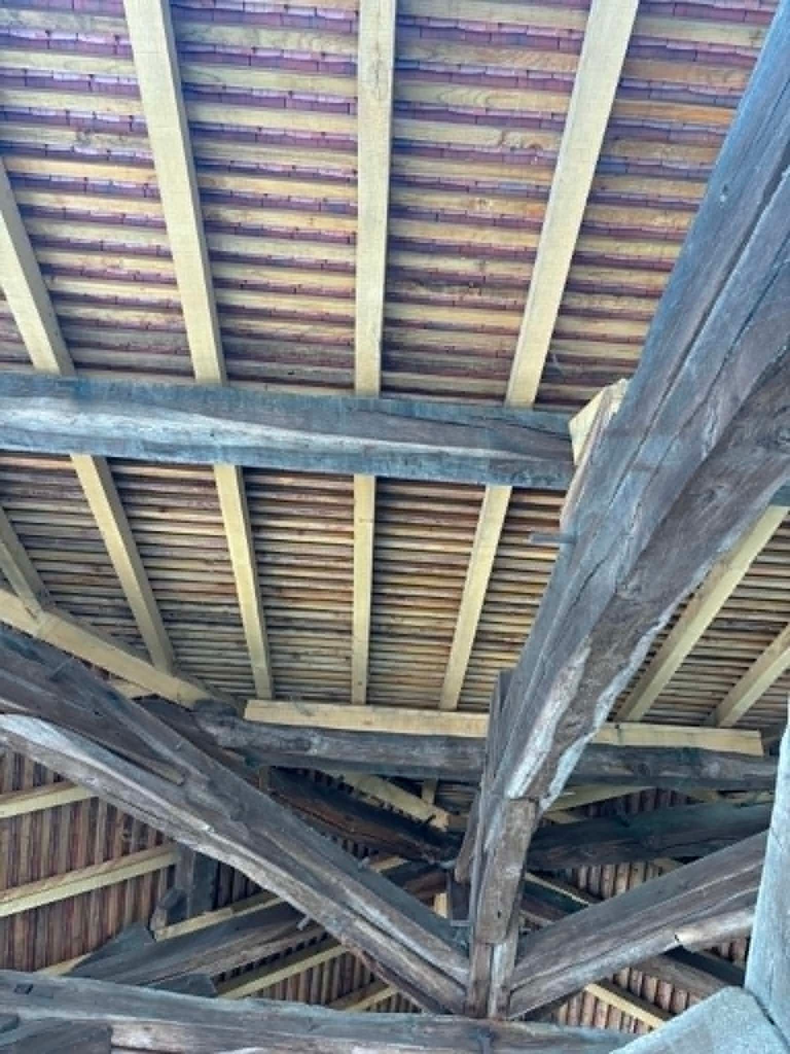 Poutres et chevrons de toiture en bois vus d'en bas, montrant les planches abîmées par les intempéries et les entretoises de soutien.