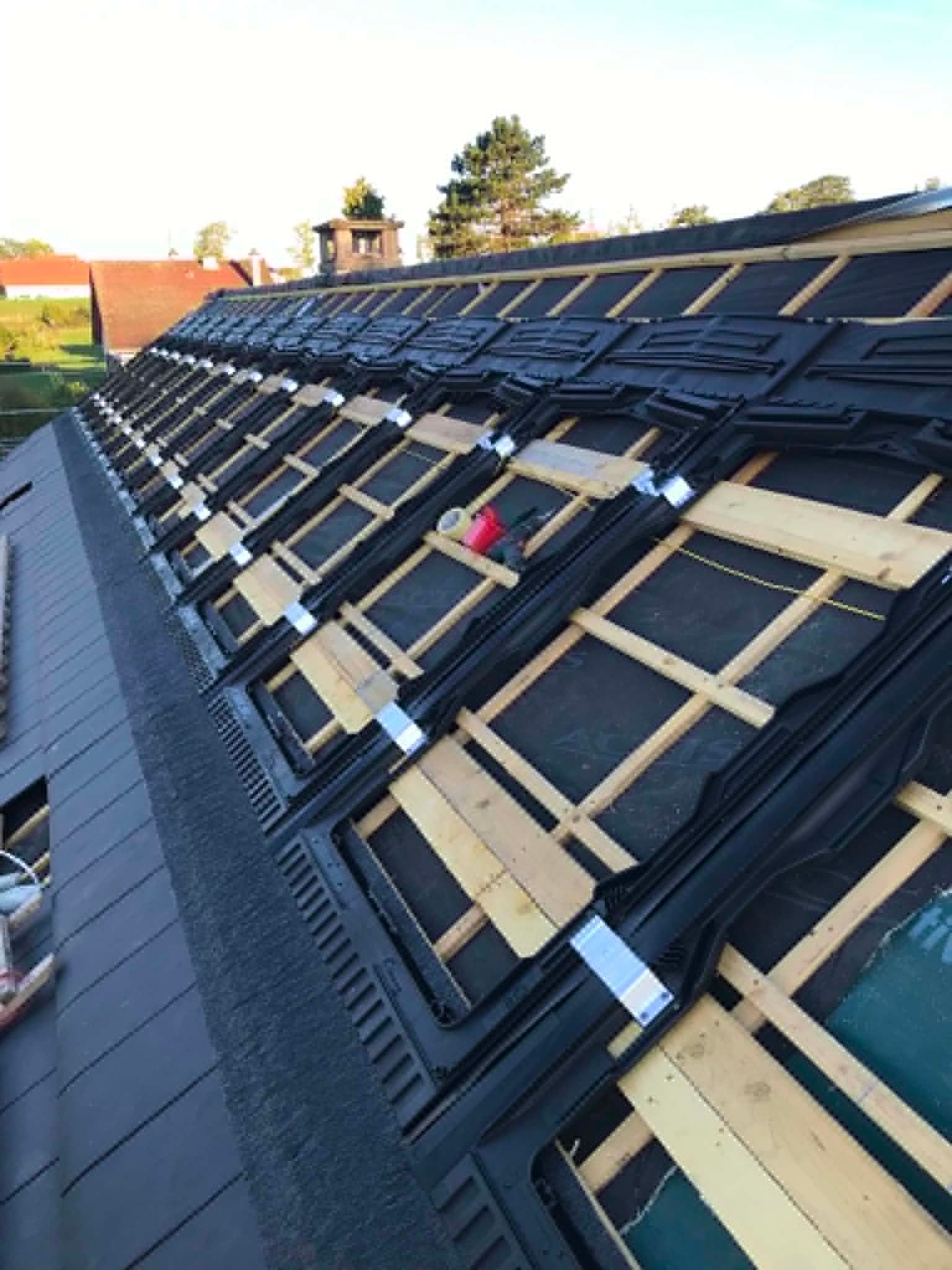 Toiture en construction avec étanchéité noire, liteaux de bois apparents et fenêtre de toit.