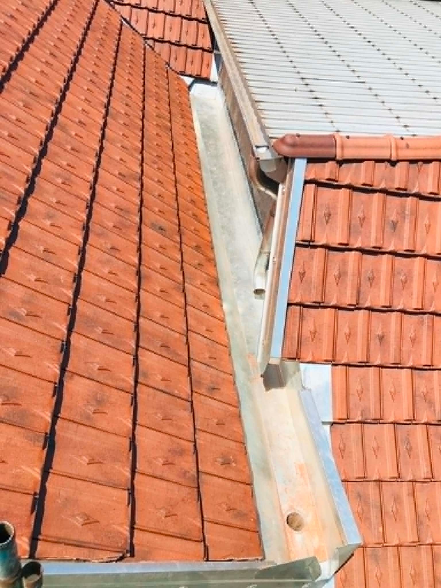 Gros plan sur des toits de tuiles rouges avec une noue métallique étroite et des solins entre elles.
