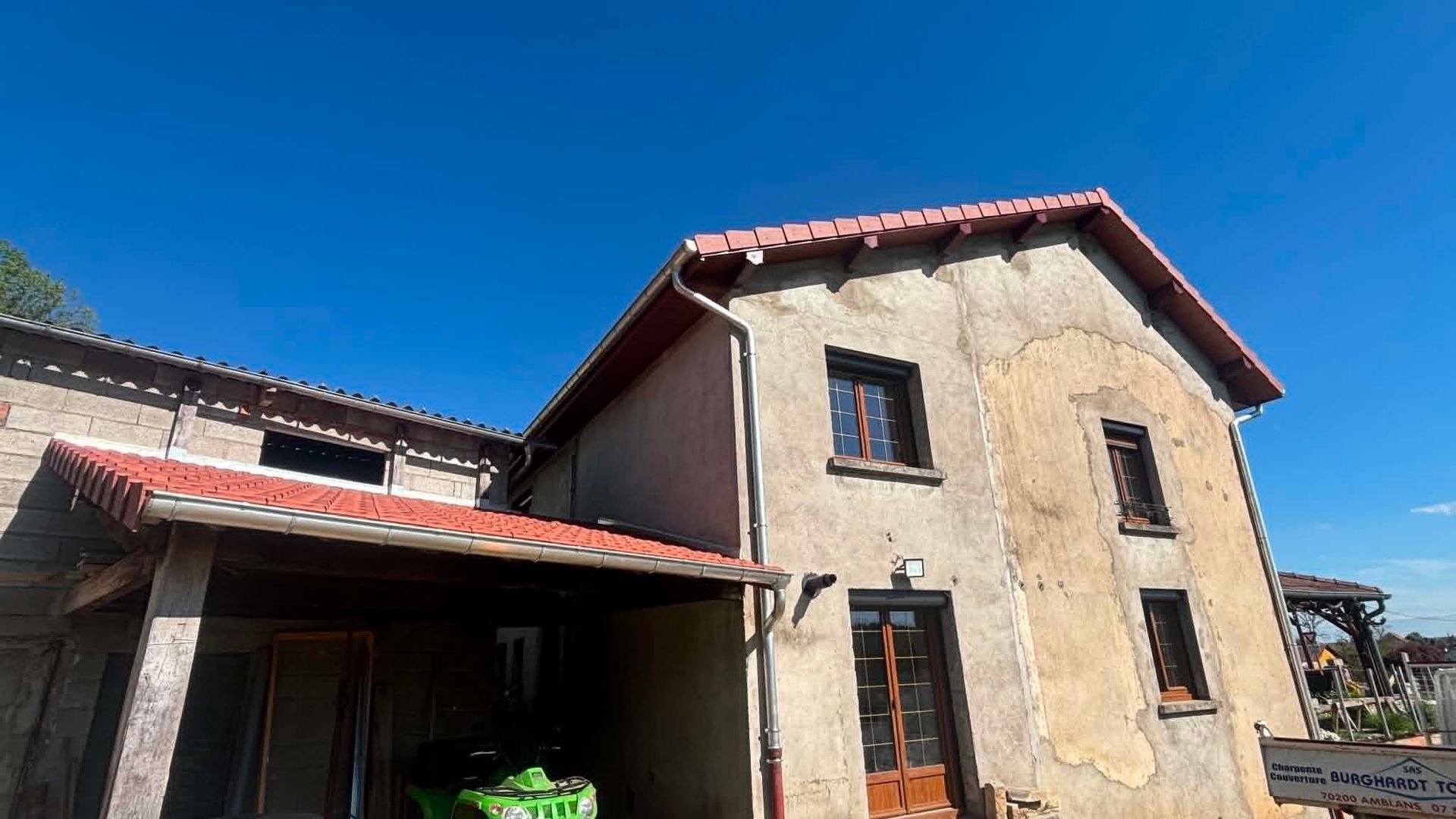 Vieille maison en stuc au toit de tuiles rouges sous un ciel d'un bleu éclatant.
