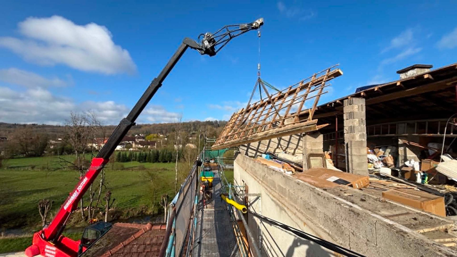 Grue soulevant des fermes de toit sur un chantier de construction à côté d'une structure en pierre partiellement construite