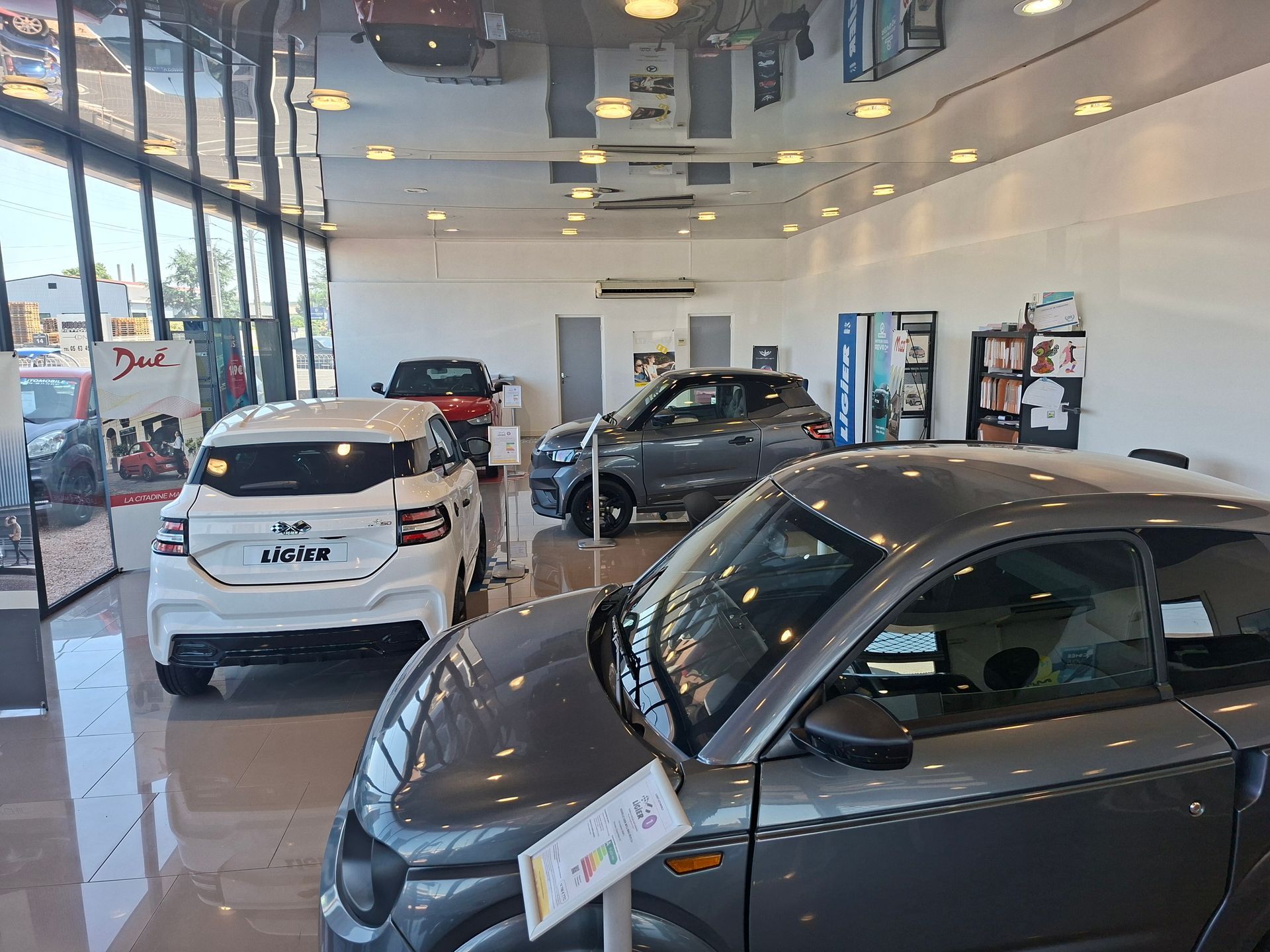 Salle d'exposition d'un concessionnaire automobile avec plusieurs voitures exposées, dont une voiture grise au premier plan.