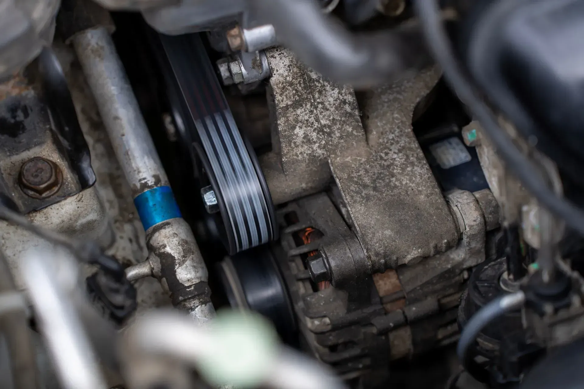 Gros plan sur une courroie de moteur et un alternateur de voiture, avec leurs tuyaux et composants métalliques.