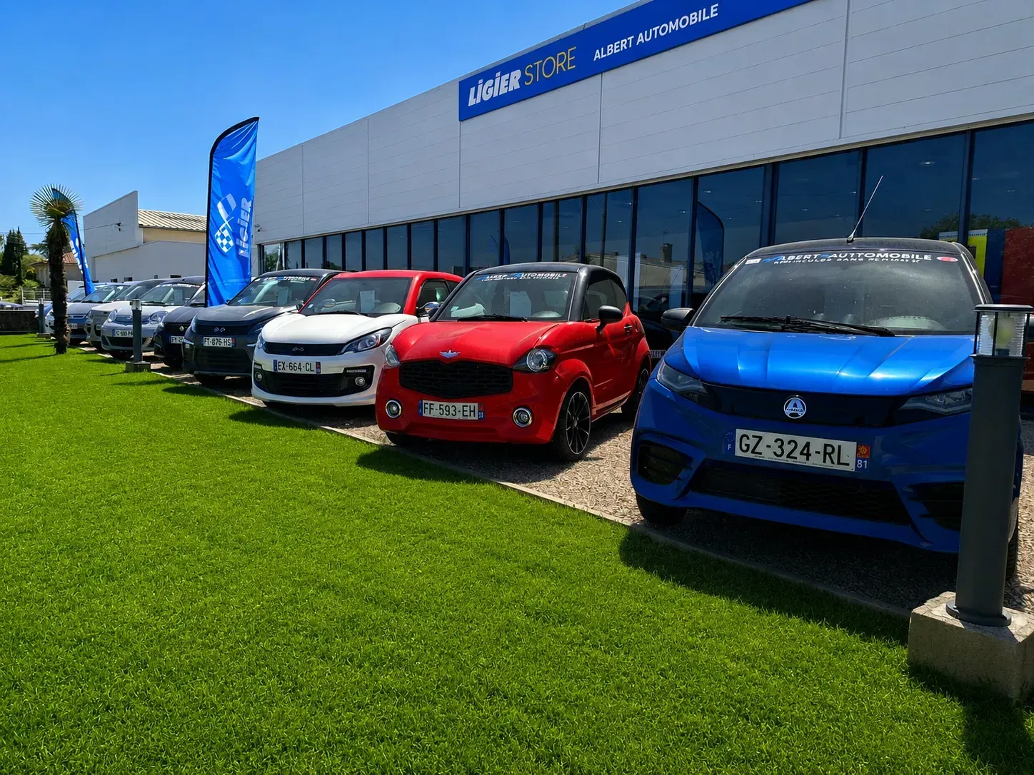 Voitures exposées devant une concession automobile, dont une voiture bleue, rouge et blanche par une journée ensoleillée.