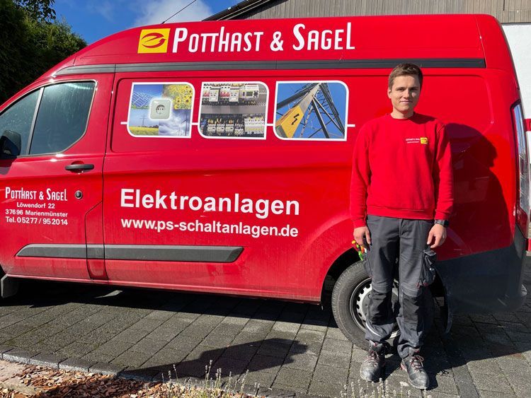 Ein Mann in roter Uniform steht neben einem roten Lieferwagen mit Firmenlogo.