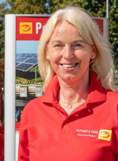 Frau lächelt, trägt ein rotes Poloshirt, hinter ihr ist das Logo von 