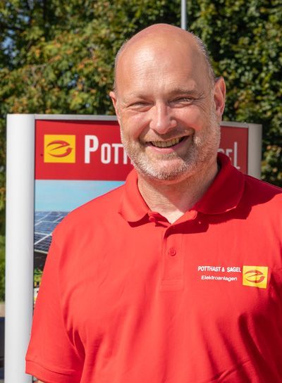 Ein Mann in einem roten Poloshirt lächelt vor einem Schild mit einem Logo und dem Wort „Potthoff“.