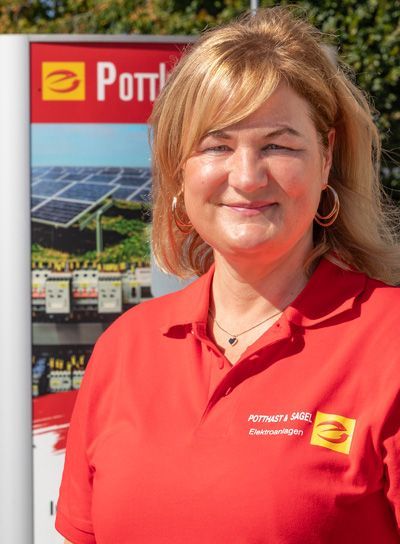 Eine Frau in einem roten Poloshirt lächelt vor einem Pöttinger-Schild und Solarpaneelen.