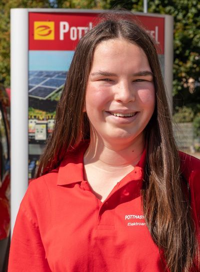 Eine Person mit Zahnspange in einem roten Poloshirt steht vor einem Tankstellenschild.
