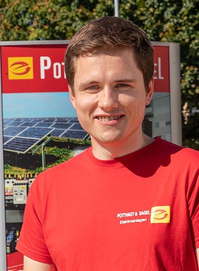 Mann in rotem Hemd lächelt vor einem Schild mit einer Abbildung eines Solarmoduls.