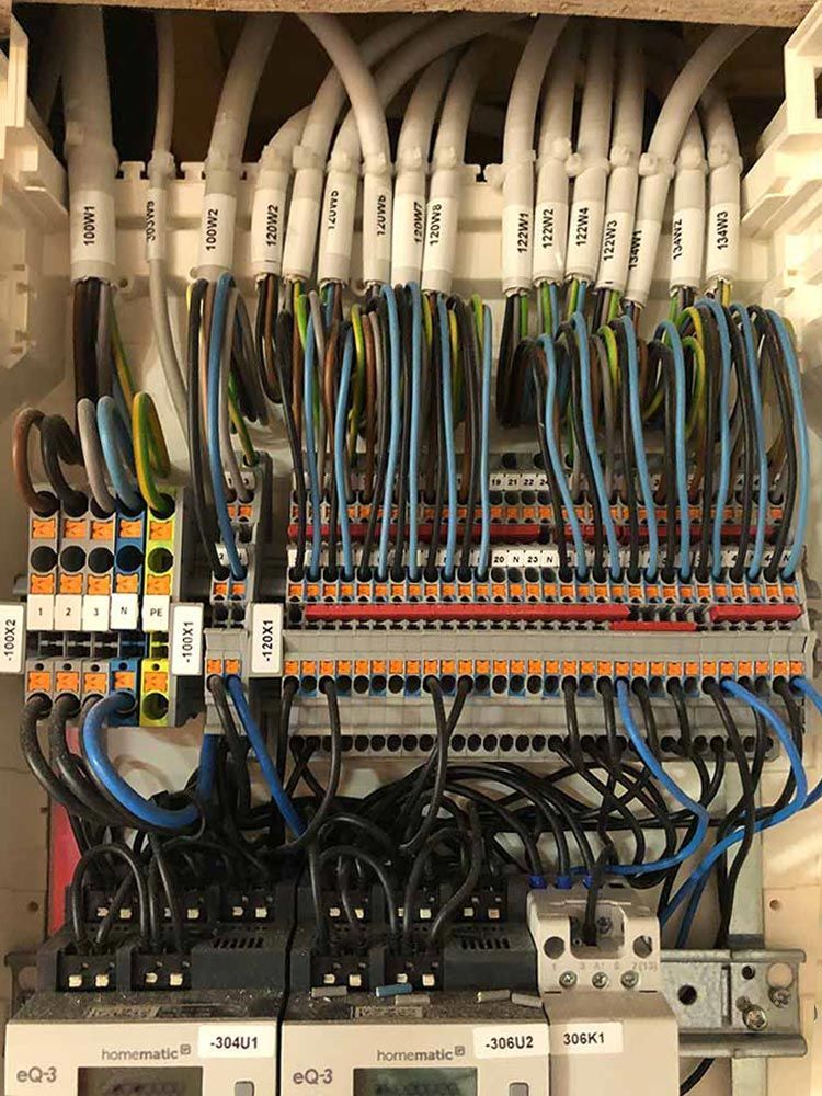 Elektrische Leitungen und Komponenten in einem Schaltschrank. Weiß Kabel werden an Klemmenblöcke und Schalter angeschlossen.