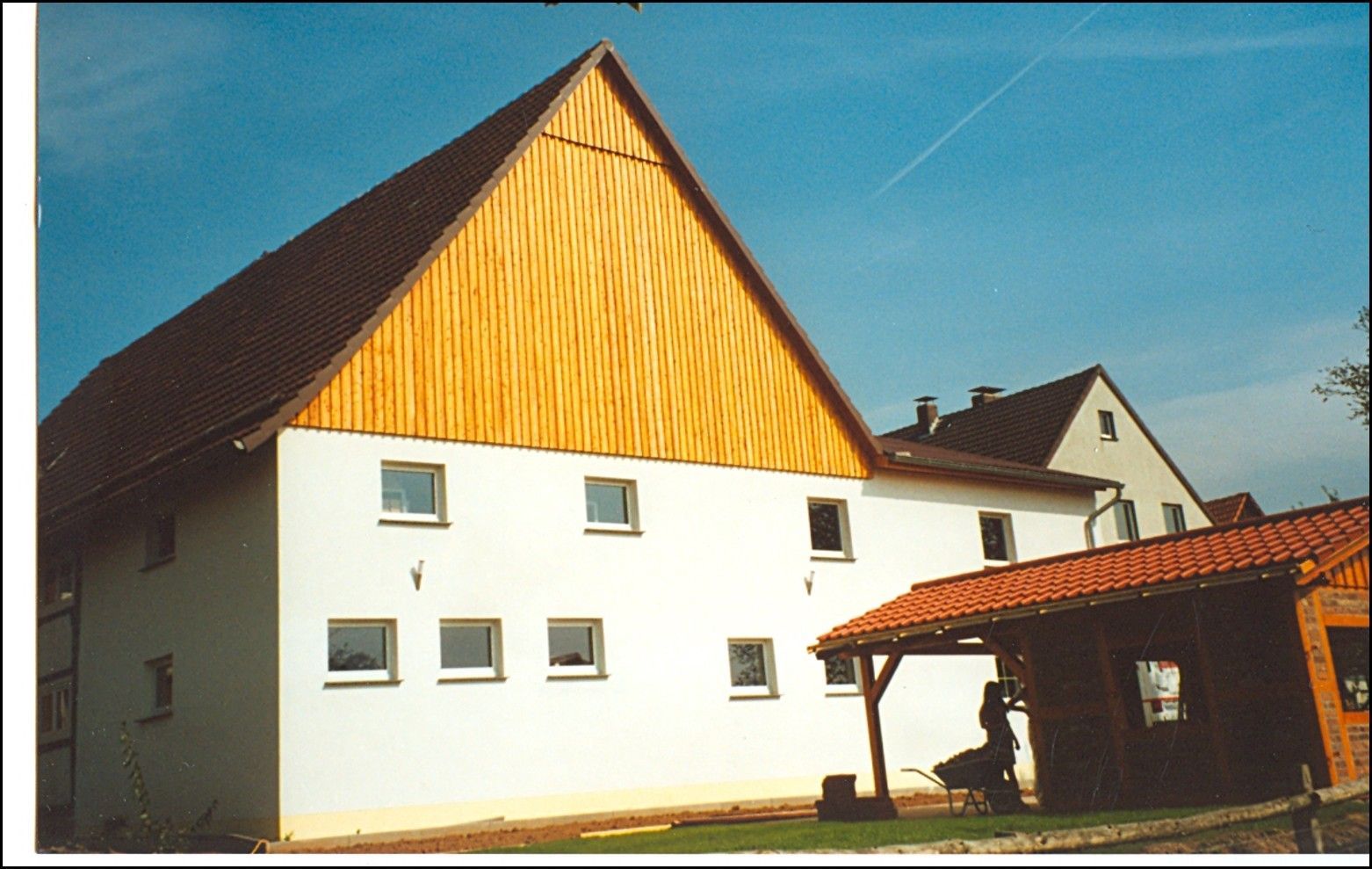 Weißes Gebäude mit braunem Dach und Holzgiebel vor blauem Himmel.