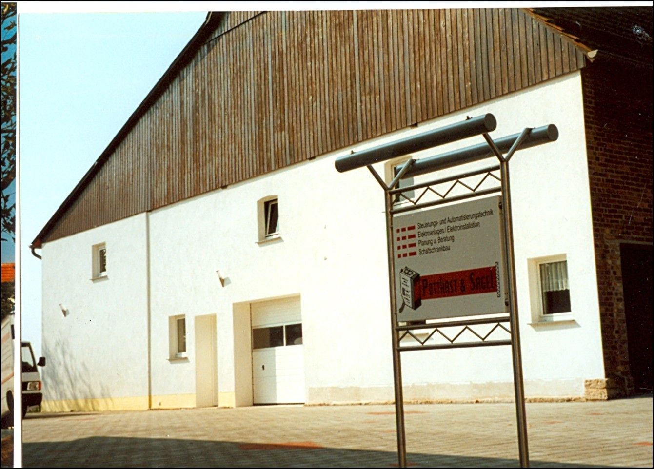 Weißes Gebäude mit brauner Holzfassade im oberen Bereich und einem Schild davor.