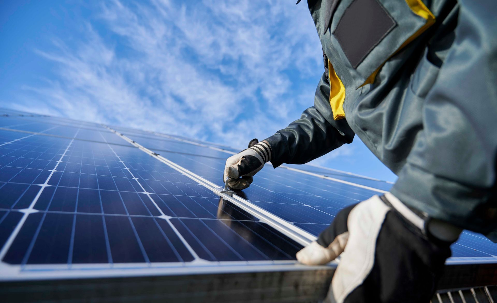 Eine Person installiert Solarpaneele auf einem Dach vor blauem Himmel.