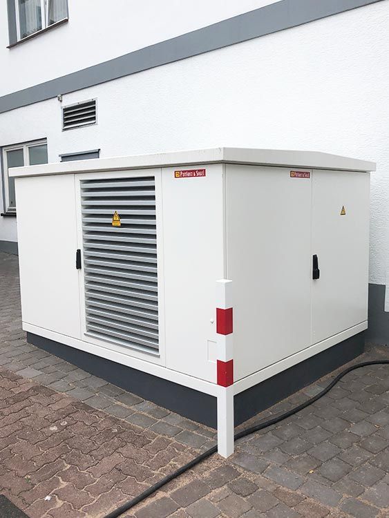 Weißer Elektroverteilerkasten mit Lamellenlüftung an einem Gebäude.