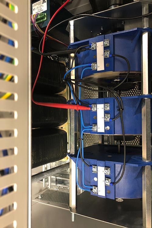 Elektrische Bauteile im Inneren eines Schaltschranks; eine Prüfspitze berührt ein Bauteil. Kabel und Lüfter sind sichtbar.