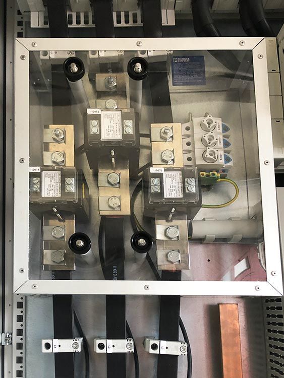 Elektrische Bauteile hinter einer transparenten Schutzabdeckung; Kupferschienen, Schraubverbinder und Verkabelung.