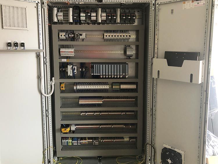 Elektrischer Schaltschrank mit verschiedenen Bauteilen, Kabeln und Sicherungsautomaten. Graues Metallgehäuse.