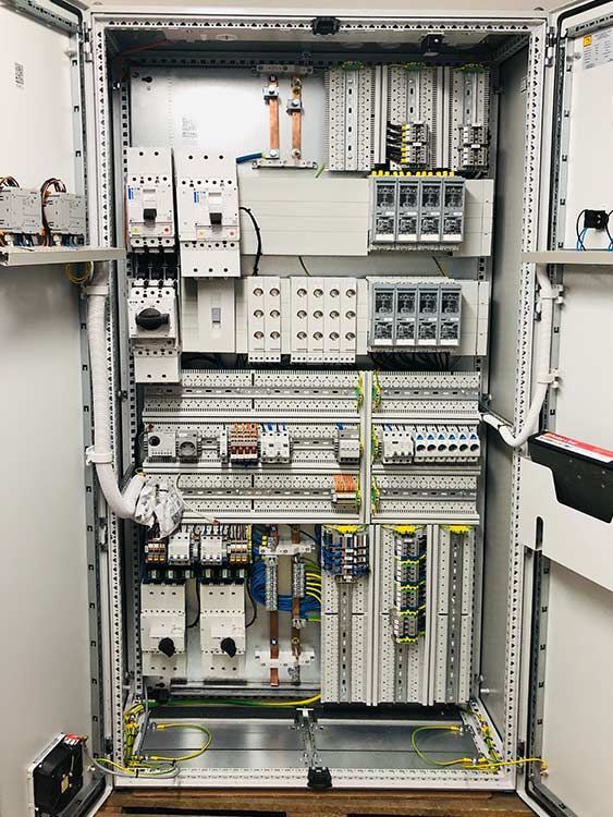 Elektrischer Schaltschrank mit verschiedenen Leistungsschaltern, Relais und Verkabelung, montiert in einem Metallgehäuse.
