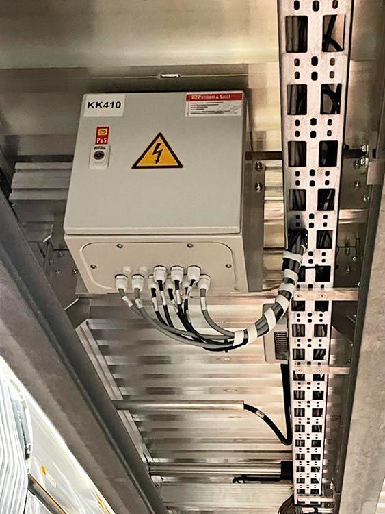 Elektroverteilerkasten mit Warnsymbol, auf Metallkonstruktion montiert, Kabel angeschlossen.