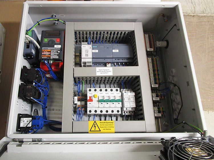 Schaltschrank mit elektrischen Bauteilen in einem weißen Gehäuse. Kabel, Leistungsschalter und eine SPS sind sichtbar.