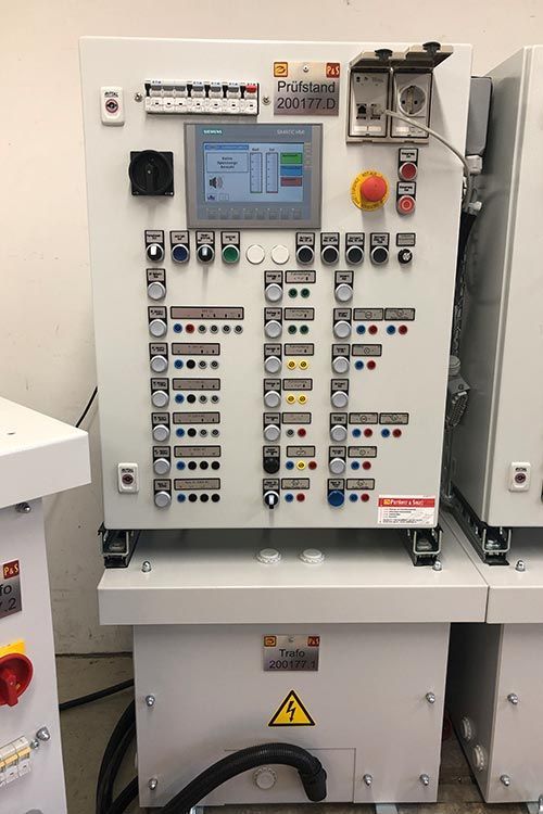 Bedienfeld mit Tasten, Display und elektrischen Bauteilen. Grau mit roten, gelben und blauen Indikatoren.