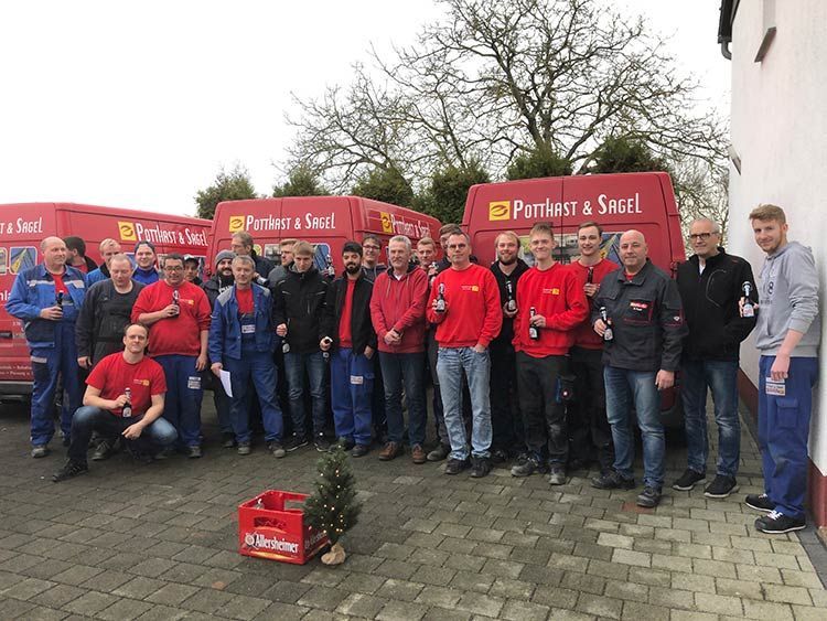 Eine Gruppe Männer in roten Hemden und Arbeitskleidung mit Lieferwagen. Viele halten Getränke in der Hand