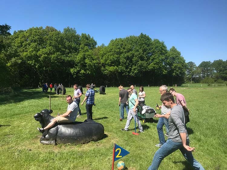 Menschen spielen an einem sonnigen Tag im Freien Minigolf. Eine Person sitzt auf einer Kuhstatue.