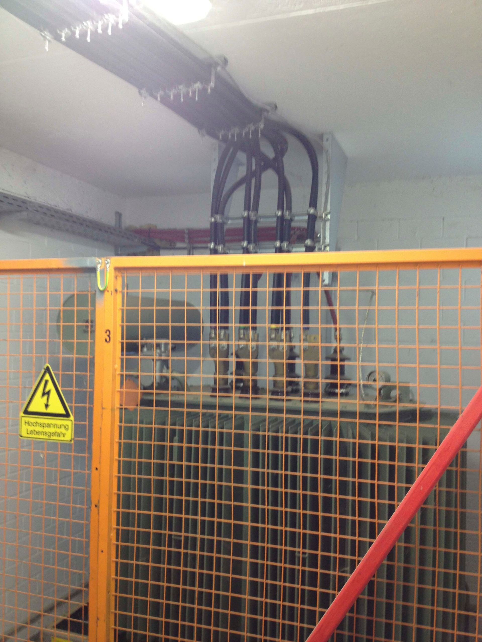 Ein Transformator befindet sich hinter einem orangefarbenen Sicherheitskäfig in einem Raum mit elektrischer Verkabelung